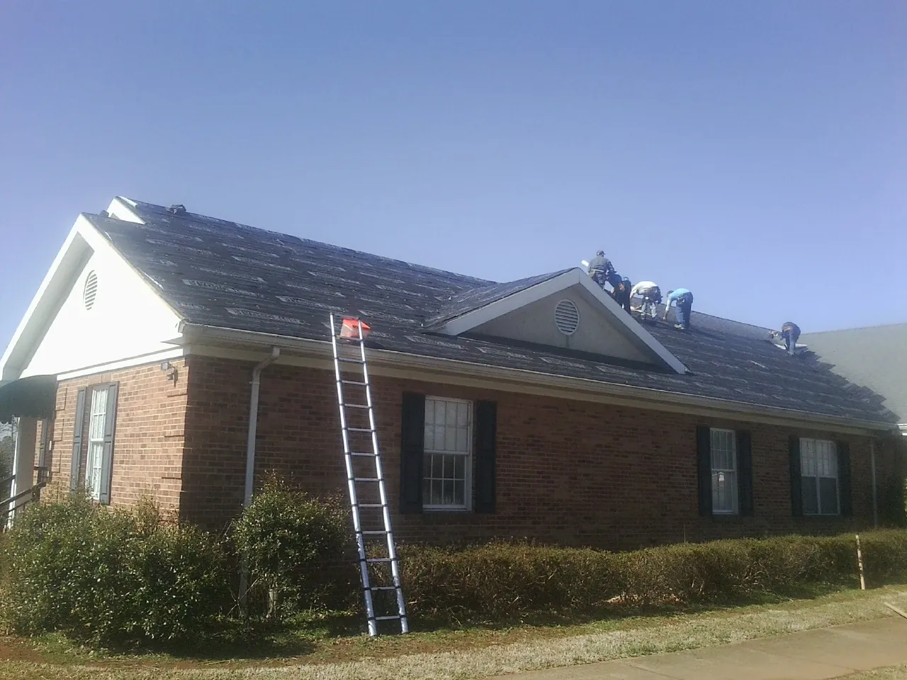 Crew tearing shingles off a brick ranch roof with a ladder set — Emergency Roof Repair work by our crew in Rockland
