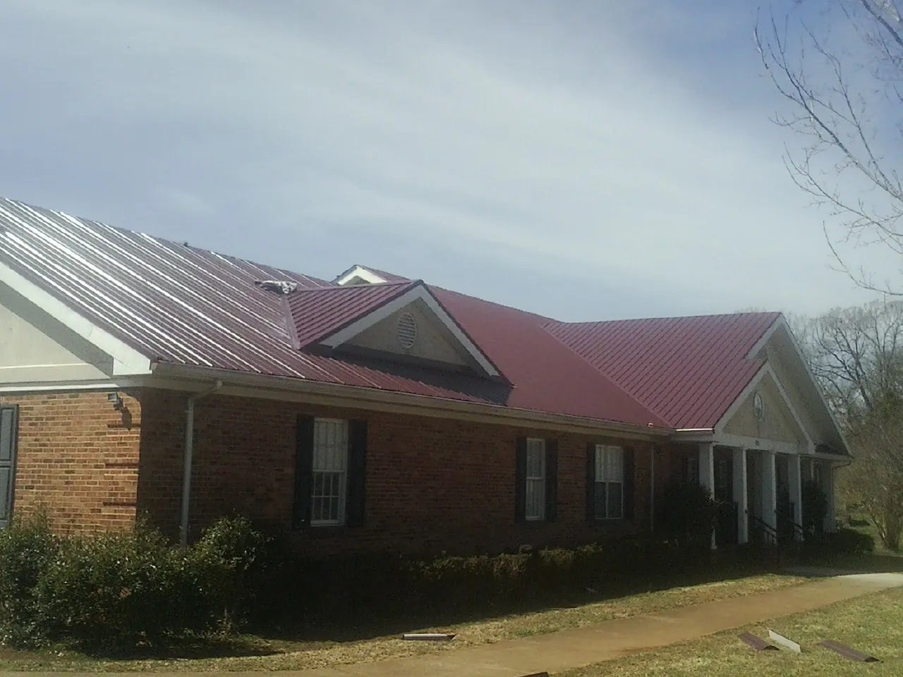 Red metal roof with gabled entries on a long brick building, from a Hail Damage Roof Repair job in Rockland